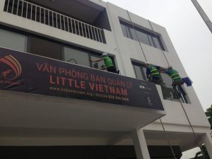 Đội ngũ kỹ thuật đang sử dụng xe nâng để vệ sinh biển hiệu Alu lớn cho một showroom ô tô tại trung tâm Hạ Long.